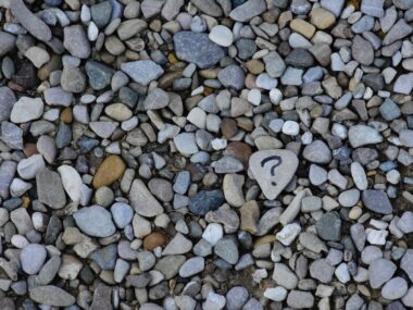 question / Muscular Dystrophy News / Photo of a bunch of small rocks. A gray one in the center has a question mark on it.