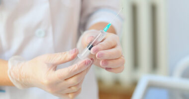 person in lab coat wearing gloves holding a syringe