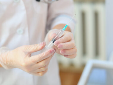 person in lab coat wearing gloves holding a syringe