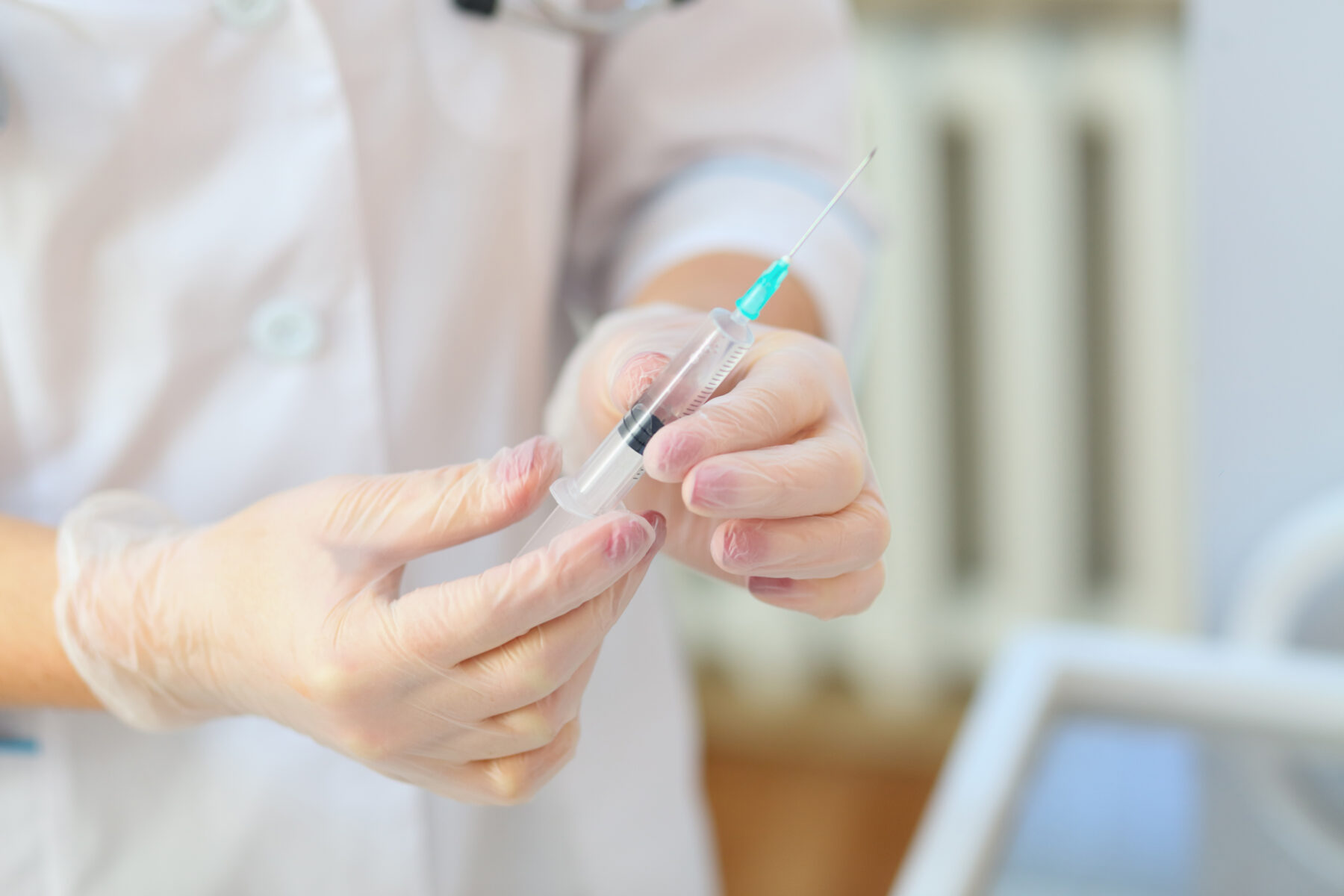 person in lab coat wearing gloves holding a syringe