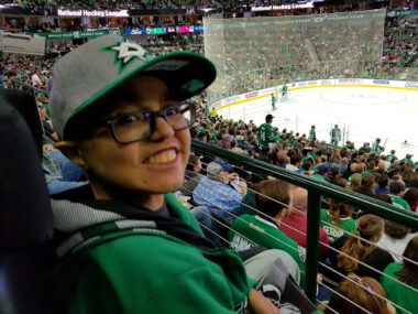 A young man smiles as a game of hockey plays in front of him.
