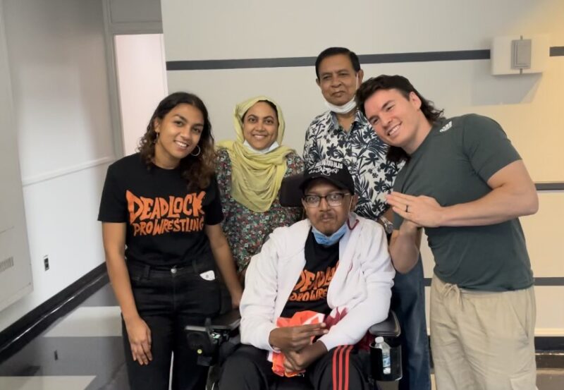A family of four poses for a photo with a wrestler.