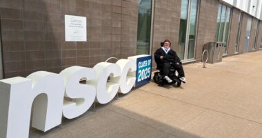 Brayden Cream sits in his power wheelchair outside the Rath Eastlink Community Centre after his college graduation, beside a sign that reads “NSCC Class of 2025.”