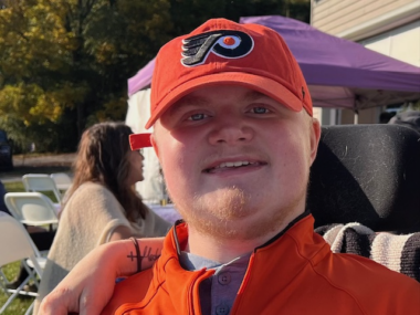 A close-up photo shows a man wearing a Philadelphia Flyers baseball cap.
