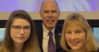 A husband, wife, and daughter pose in dress clothes in a static shot.