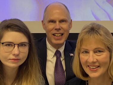 A husband, wife, and daughter pose in dress clothes in a static shot.