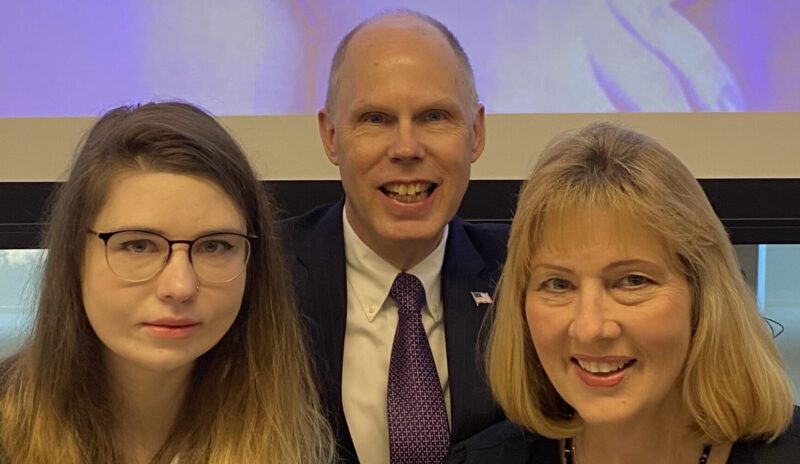 A husband, wife, and daughter pose in dress clothes in a static shot.