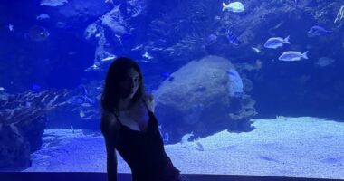 Alena Jones is seated in front of the glass of a large aquarium while vacationing in Spain.