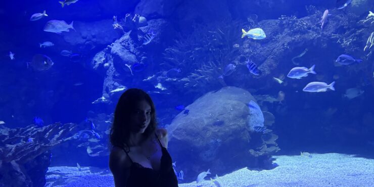 Alena Jones is seated in front of the glass of a large aquarium while vacationing in Spain.