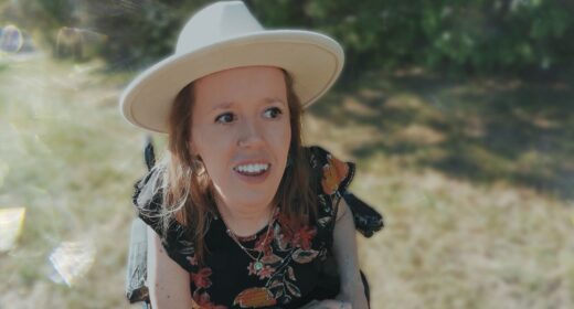 A woman wearing a wide-brimmed hat sits in her power wheelchair in a grassy park.