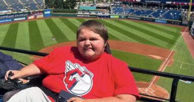 A man in a power wheelchair is seen with a professional baseball stadium behind him.