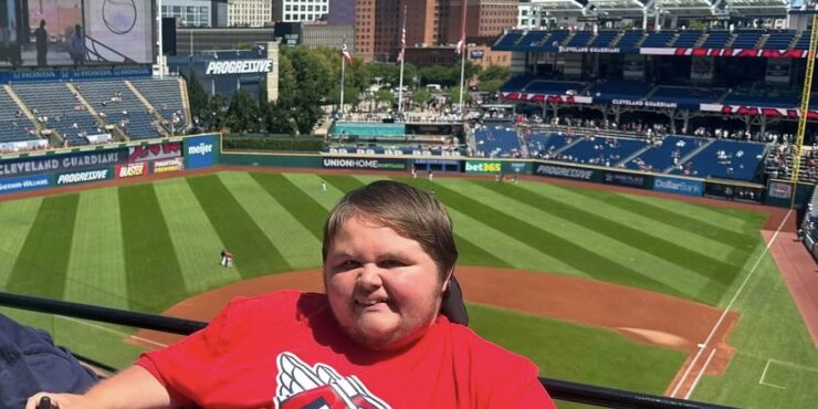 A man in a power wheelchair is seen with a professional baseball stadium behind him.