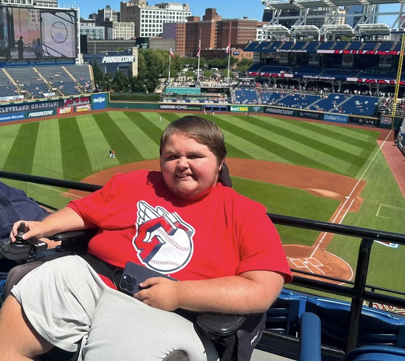 A man in a power wheelchair is seen with a professional baseball stadium behind him.