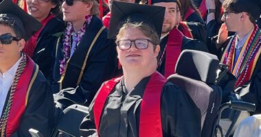 A man wearing a cap and gown is seated among other graduates.