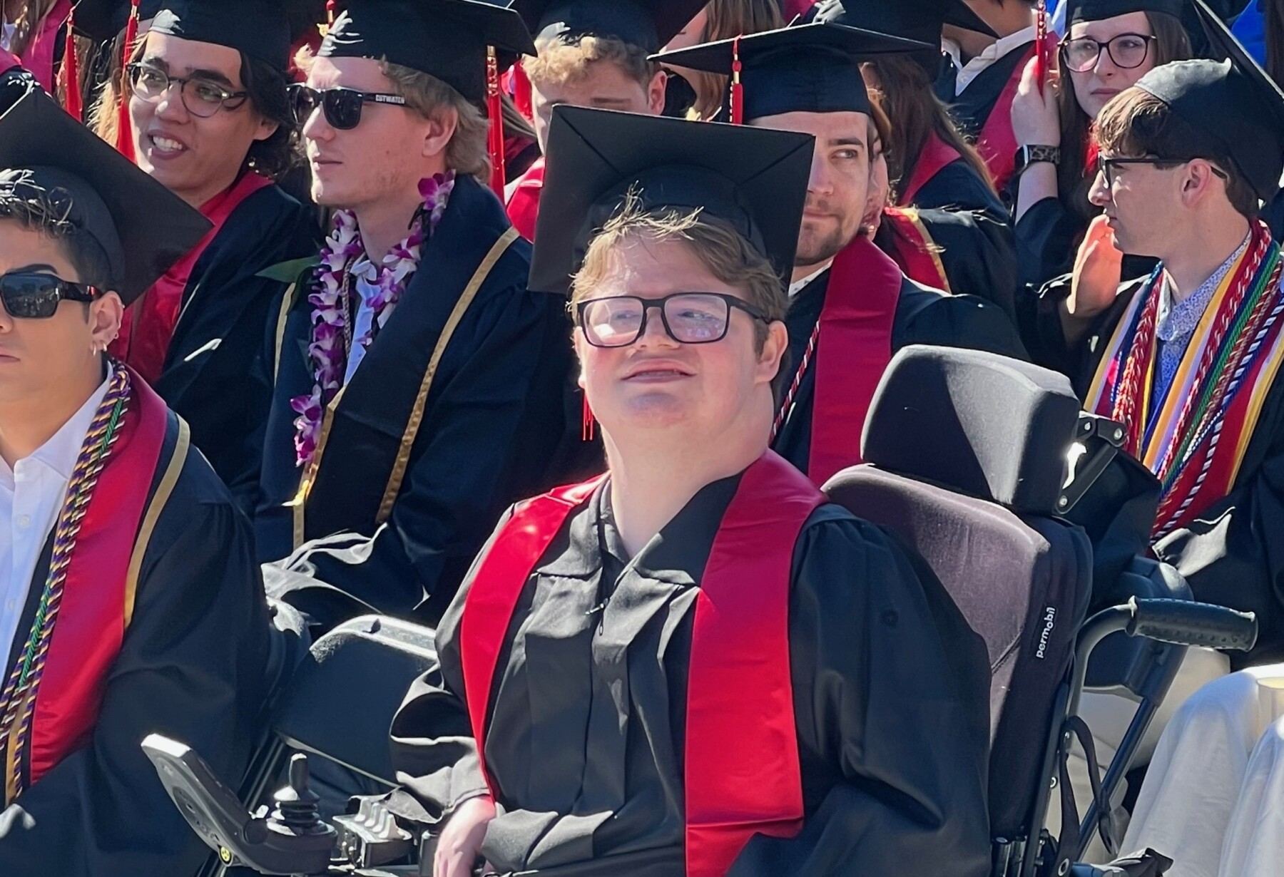 A man wearing a cap and gown is seated among other graduates.