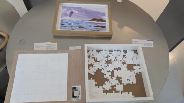 Two framed displays show tactile artwork and a painting, both sitting on round table. 